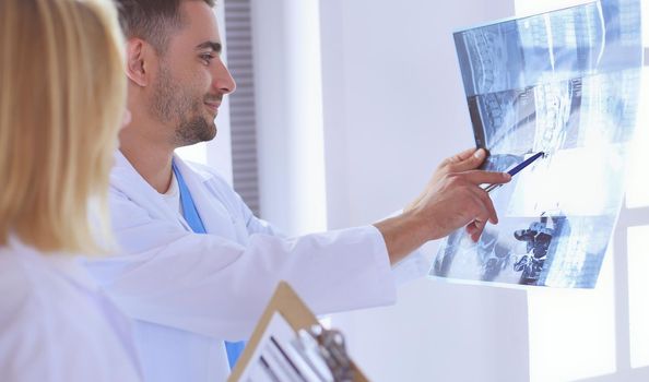 Handsome doctor is talking with young female doctor and making notes while sitting in his office