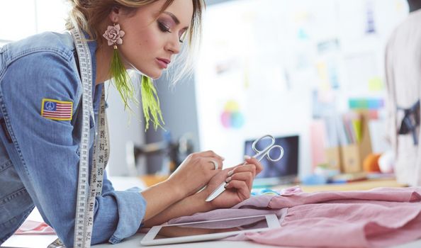 Fashion designer woman working with ipad on her designs in the studio.