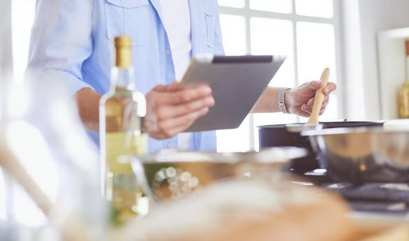 Man following recipe on digital tablet and cooking tasty and healthy food in kitchen at home.