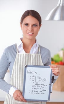 Woman in the kitchen at home, standing near desk with folder.