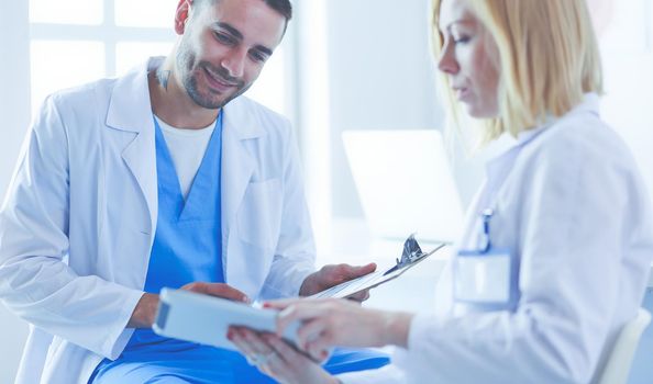 Handsome doctor is talking with young female doctor and making notes while sitting in his office