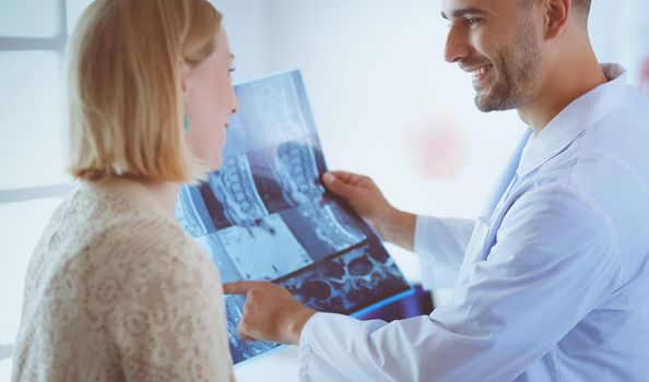 Handsome doctor is talking with young female patient and making notes while sitting in his office.