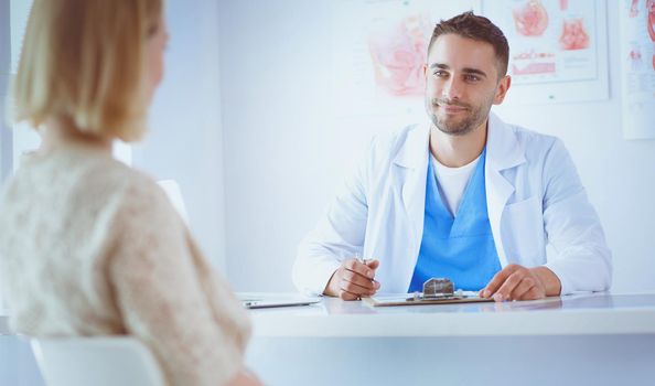 Handsome doctor is talking with young female patient and making notes while sitting in his office.