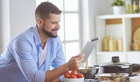 Man following recipe on digital tablet and cooking tasty and healthy food in kitchen at home.