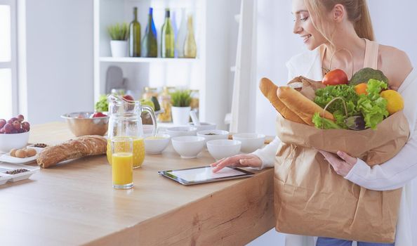 Young woman holding grocery shopping bag with vegetables .Standing in the kitchen.