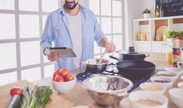 Man following recipe on digital tablet and cooking tasty and healthy food in kitchen at home.