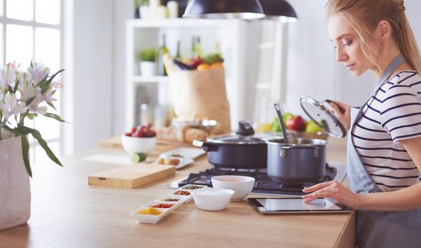 Young woman using a tablet computer to cook in her kitchen.