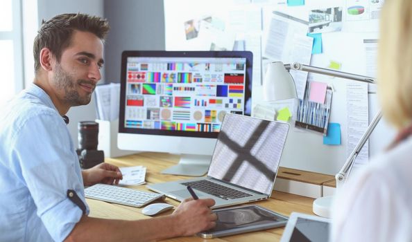 Portrait of young designer sitting at graphic studio in front of laptop and computer while working online