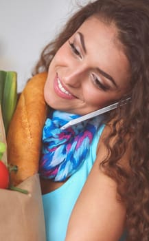 SmiSmiling woman with mobile phone holding shopping bag in kitchenling woman with mobile phone holding shopping bag in kitchen