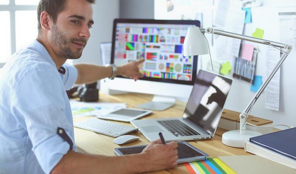 Portrait of young designer sitting at graphic studio in front of laptop and computer while working online