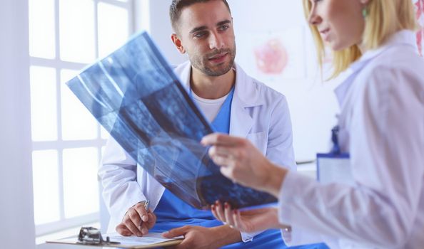 Handsome doctor is talking with young female doctor and making notes while sitting in his office