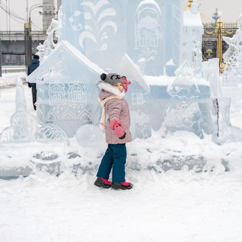 a little girl in winter clothes near the ice sculptures. the child walks in the winter in the park, snow-covered town.