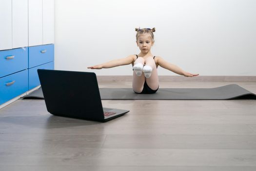 child girl in a gymnastic leotard is engaged in fitness with a trainer online.