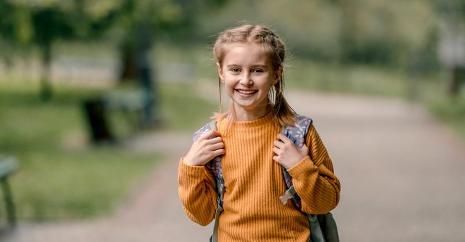 Pretty school girl with backpack looking at camera and smiling. Carefree child kid at autumn outdoors portrait