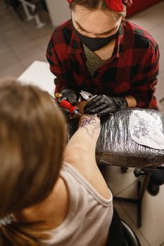 Professional tattoo master making tattoo on client body wering gloves and protective mask