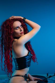 a girl with a chic hairstyle in exciting latex clothes and stockings is sitting on the floor with a leather rose in her hands