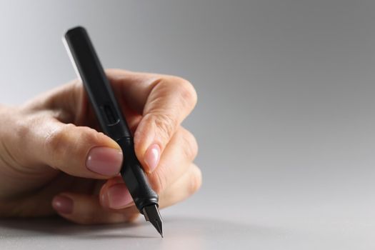 Close-up of person holding black feather pen, sharp tip, tool for writing. Pen on grey surface. Stationery, writing, office supplies concept. Copy space