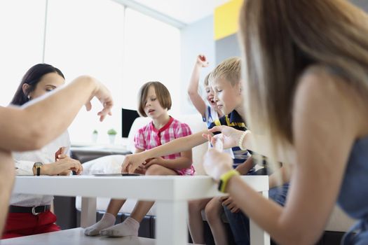 Portrait of group of children spend time in kindergarten with teacher or mum entertain kids with card games. Childhood, fun, family, development concept