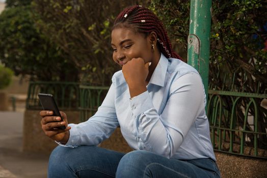 Businesswoman sitting on the street, holding hands on chin and relaxing while on smart phone outdoors