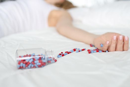 Dead woman lying on bed with scattered medical capsules closeup. Suicide concept