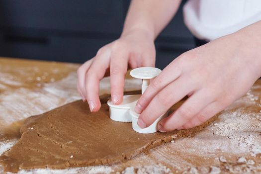 A little girl makes heart-shaped cookies from rye dough. The concept of Valentine's Day and healthy baking. Cooking cookies in close-up.