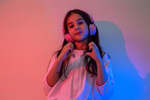 Little girl in pink headphones dancing to music in neon pink blue light