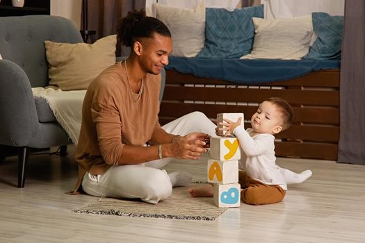 Young father and little son play cubes on the floor of the room, build a tower