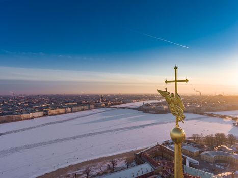 Aerial view of golden Angel and Cross on spike of the Peter and Paul cathedral in Saint Petersburg at sunset, frozen Neva River, sunny frosty day, Winter Palace, Admiralty, Rostral columns. High quality photo