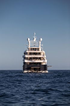 The boat stern of huge yacht in sea at sunny day, glossy board of the motor boat, the chrome plated handrail, megayacht is moored in harbour, sun reflection on glossy board. High quality photo