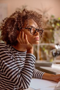 Multiracial lady in glasses resting chin on her hand and looking away with serious expression