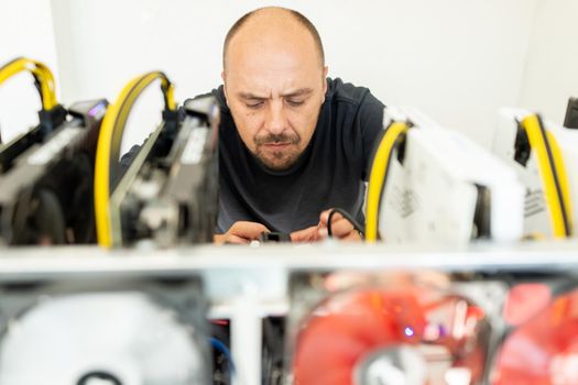 Young programmer adjusting cryptocurrency mining rig to optimal operational settings. High quality photo