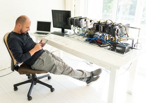 Young programmer adjusting cryptocurrency mining rig to optimal operational settings. High quality photo