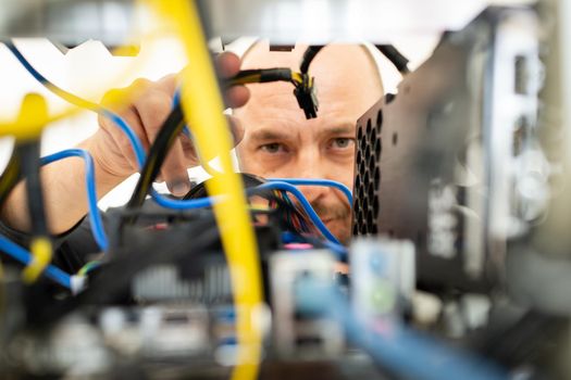 Young programmer adjusting cryptocurrency mining rig to optimal operational settings. High quality photo