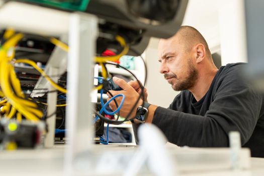 Young programmer adjusting cryptocurrency mining rig to optimal operational settings. High quality photo