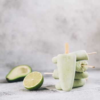 Homemade raw vegan avocado lime popsicle. Sugar-free, non-dairy green ice cream on gray cement textured background. Copy space. Ideas and recipes for healthy snack, dessert or smoothie