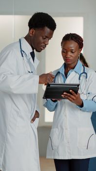 Doctors doing teamwork with digital tablet to find medicine against disease. Man and woman with gadget looking at screen to find healthcare information about treatment. Medical care