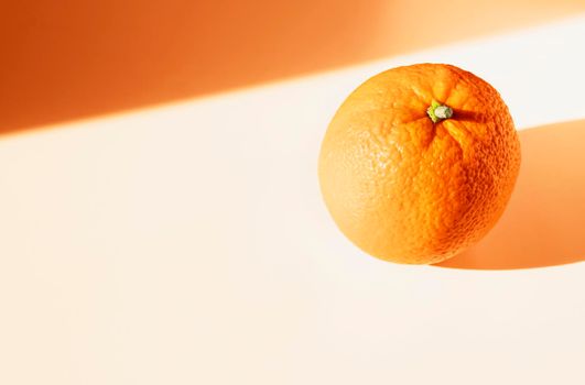 One orange fruit on white table , orange colored shadows , 