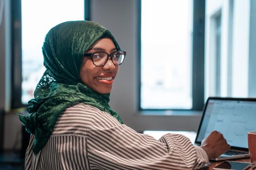 Businesswoman wearing a green hijab using laptop in relaxation area at modern open plan startup office. Selective focus. High-quality photo