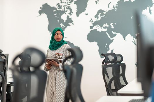 Portrait of Muslim female software developer with green hijab holding tablet computer while standing at modern open plan startup office. High-quality photo