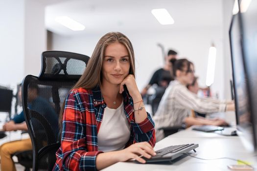 Casual businesswoman working on a desktop computer in modern open plan startup office interior. Selective focus. High-quality photo
