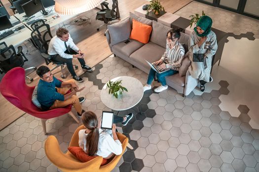 Top view photo of Multiethnic startup business team having brainstorming in relaxation area of modern office interior working on laptop and tablet computer. High-quality photo