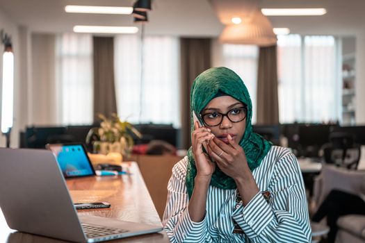 Smiling young woman talk on smartphone work on laptop look in distance thinking. Happy African American customer client using modern gadgets cellphone and computer at the home office. High-quality photo