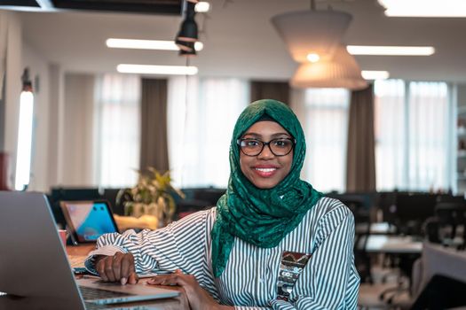 Businesswoman wearing a green hijab using laptop in relaxation area at modern open plan startup office. Selective focus. High-quality photo