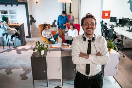 Portrait of successful businessman entrepreneur with headphones around his neck and colleagues in the background at busy startup office. High-quality photo