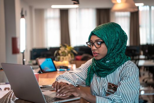 Businesswoman wearing a green hijab using laptop in relaxation area at modern open plan startup office. Selective focus. High-quality photo