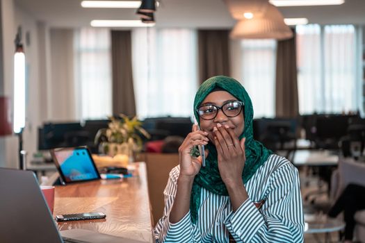 Smiling young woman talk on smartphone work on laptop look in distance thinking. Happy African American customer client using modern gadgets cellphone and computer at the home office. High-quality photo