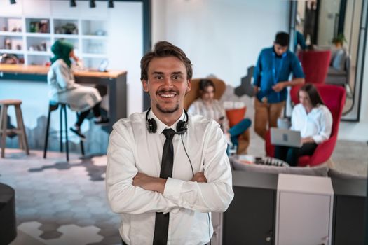 Portrait of successful businessman entrepreneur with headphones around his neck and colleagues in the background at busy startup office. High-quality photo