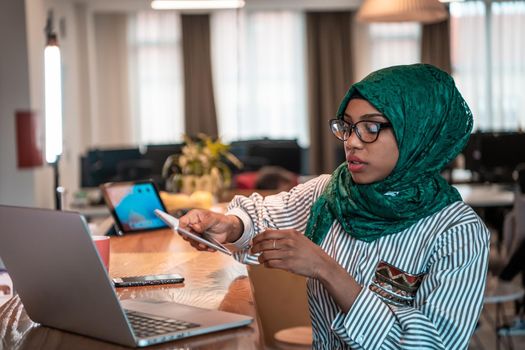 Smiling young woman talk on smartphone work on laptop look in distance thinking. Happy African American customer client using modern gadgets cellphone and computer at the home office. High-quality photo