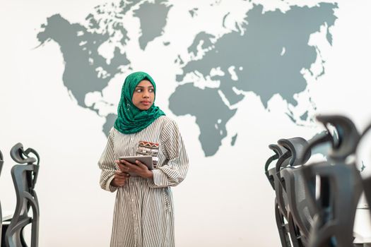 Portrait of Muslim female software developer with green hijab holding tablet computer while standing at modern open plan startup office. High-quality photo