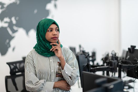 Portrait of Muslim black female software developer with green hijab standing at modern open plan startup office. Selective focus. High-quality photo